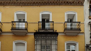 A yellow building with three balconies, white window frames, and a decorative cornice. - Central Apartment in Seville (Sevilla)