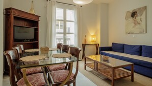 A living room with a glass dining table, wooden chairs, a blue sofa, a television, and a painting on the wall. - Central Apartment in Seville (Sevilla)