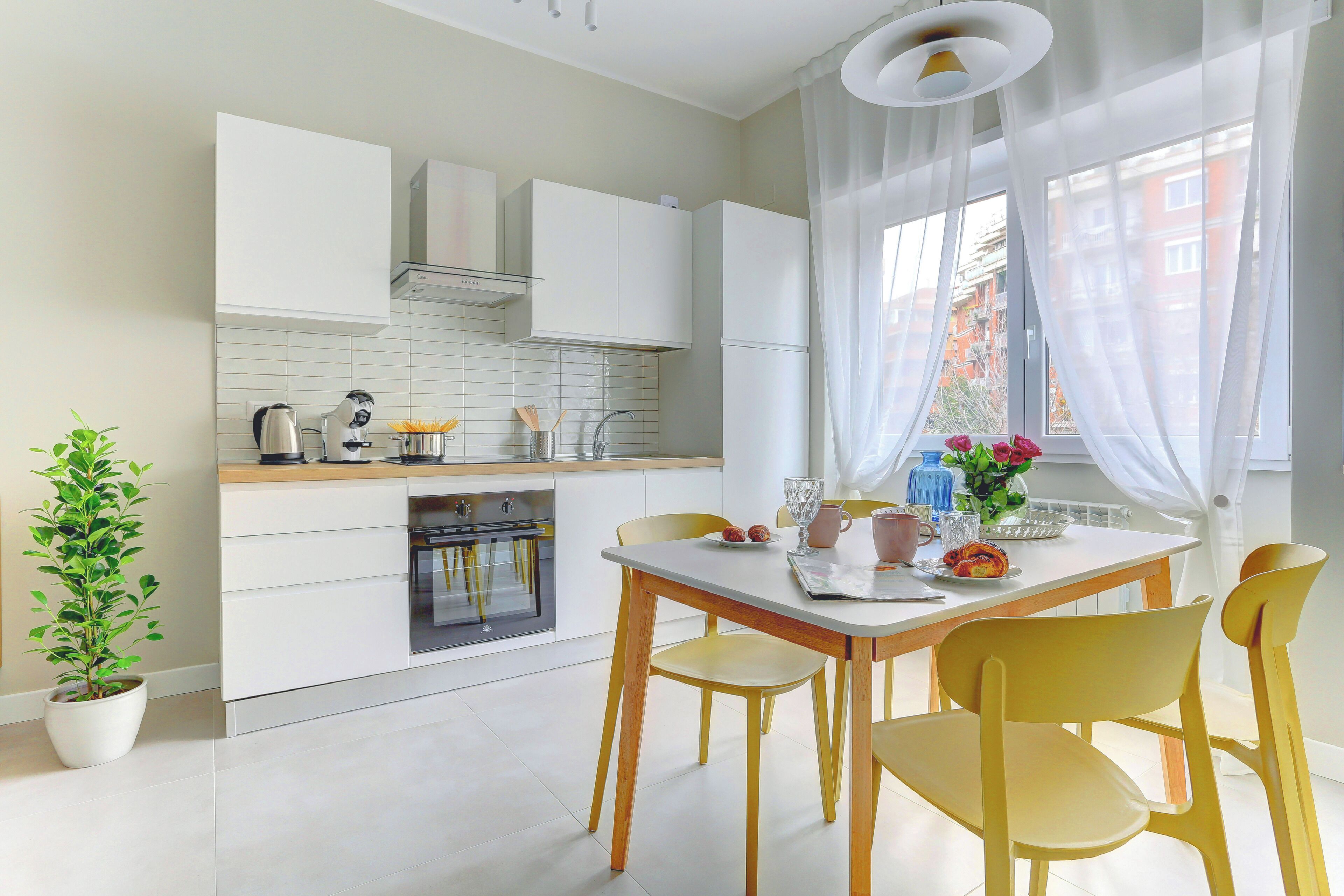 A modern kitchen with white cabinets, a built-in oven, and a dining area with a table and chairs.