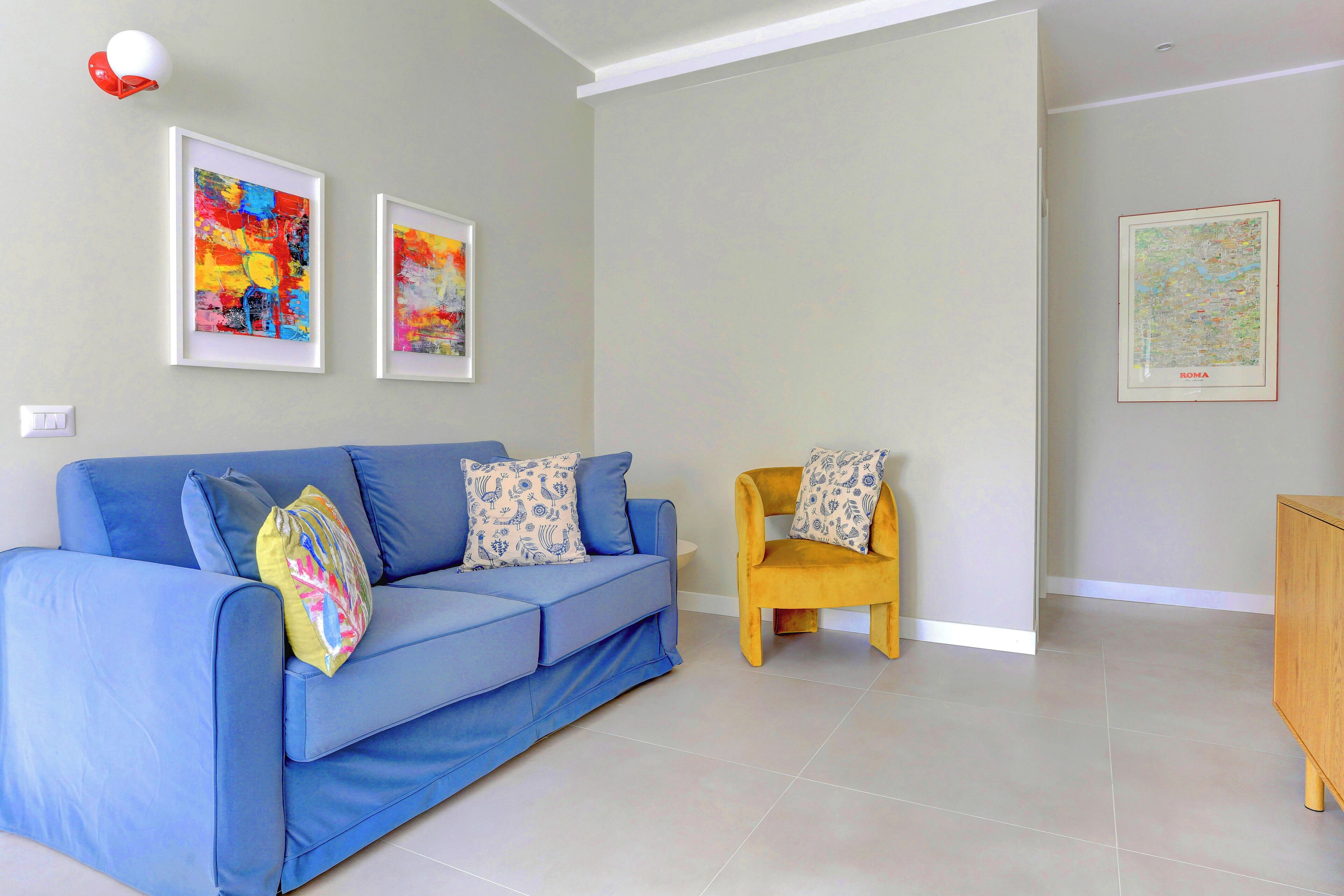 A living room with a blue sofa, a yellow armchair, and two framed abstract paintings on the wall.
