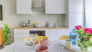 Cozinha moderna com armários brancos, coifa de aço inoxidável e bancada com cafeteira e utensílios.