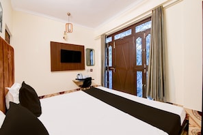A hotel room with a bed, a TV, a mirror, a window with curtains, and a door with a decorative glass panel. - Classic With Balconyhotel Parv (Varanasi)