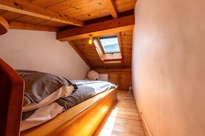 Quarto em sótão de madeira com teto inclinado, claraboia, cama e um urso de pelúcia.