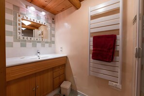Casa de banho com toucador de madeira, espelho com moldura decorativa, porta-toalhas com toalha vermelha e radiador branco.