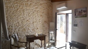 Una habitación con pared de piedra, vigas de madera en el techo, un escritorio con espejo, una silla y una cama.