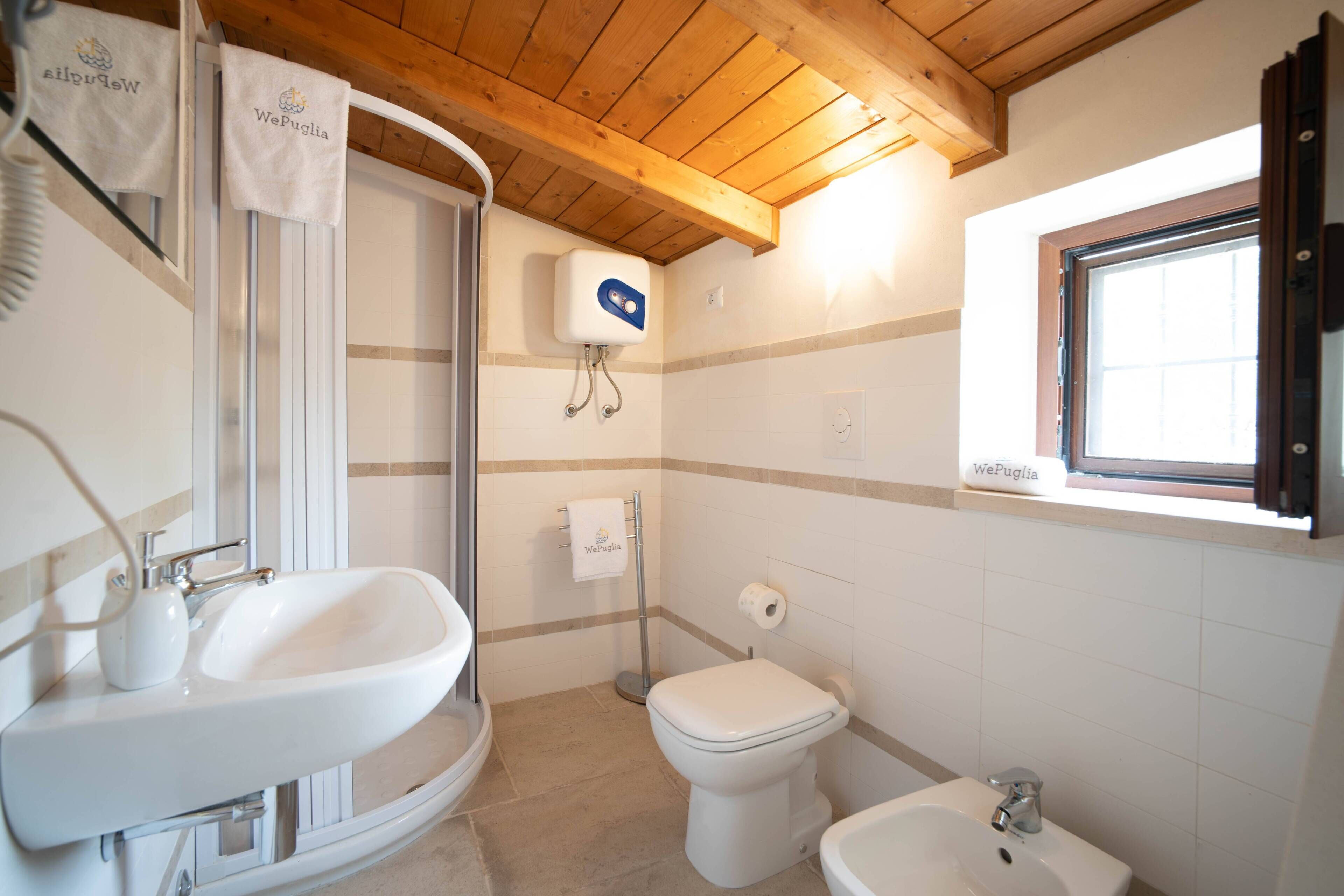 A bathroom with a sink, toilet, bidet, and a window.