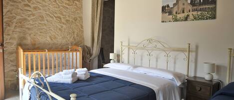 A bedroom with a stone wall, a bed with a headboard, a nightstand with a lamp, and a painting on the wall.