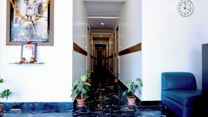 Un hall d’hôtel avec un sol en marbre, un fauteuil bleu, une horloge et un tableau encadré au mur.