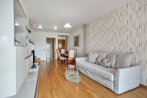 Een moderne woonkamer met een bank, een glazen salontafel en een eethoek met stoelen en een tafel.