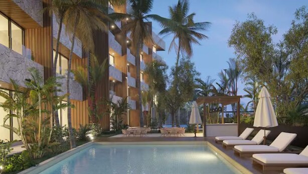 A swimming pool with lounge chairs and a covered seating area, surrounded by palm trees and a building with wooden paneling. - Sleek New Condo with Island Charm in Cozumel (Cozumel)