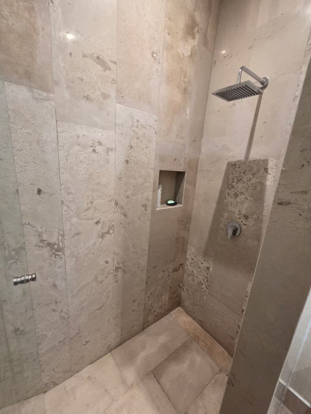 A shower with a handheld showerhead, a small shelf, and a door with a lock.