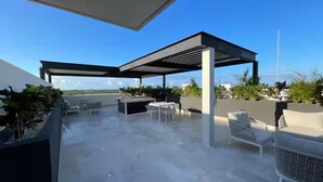 An outdoor patio with a pergola, seating, and a view of the landscape. - Sleek New Condo with Island Charm in Cozumel (Cozumel)