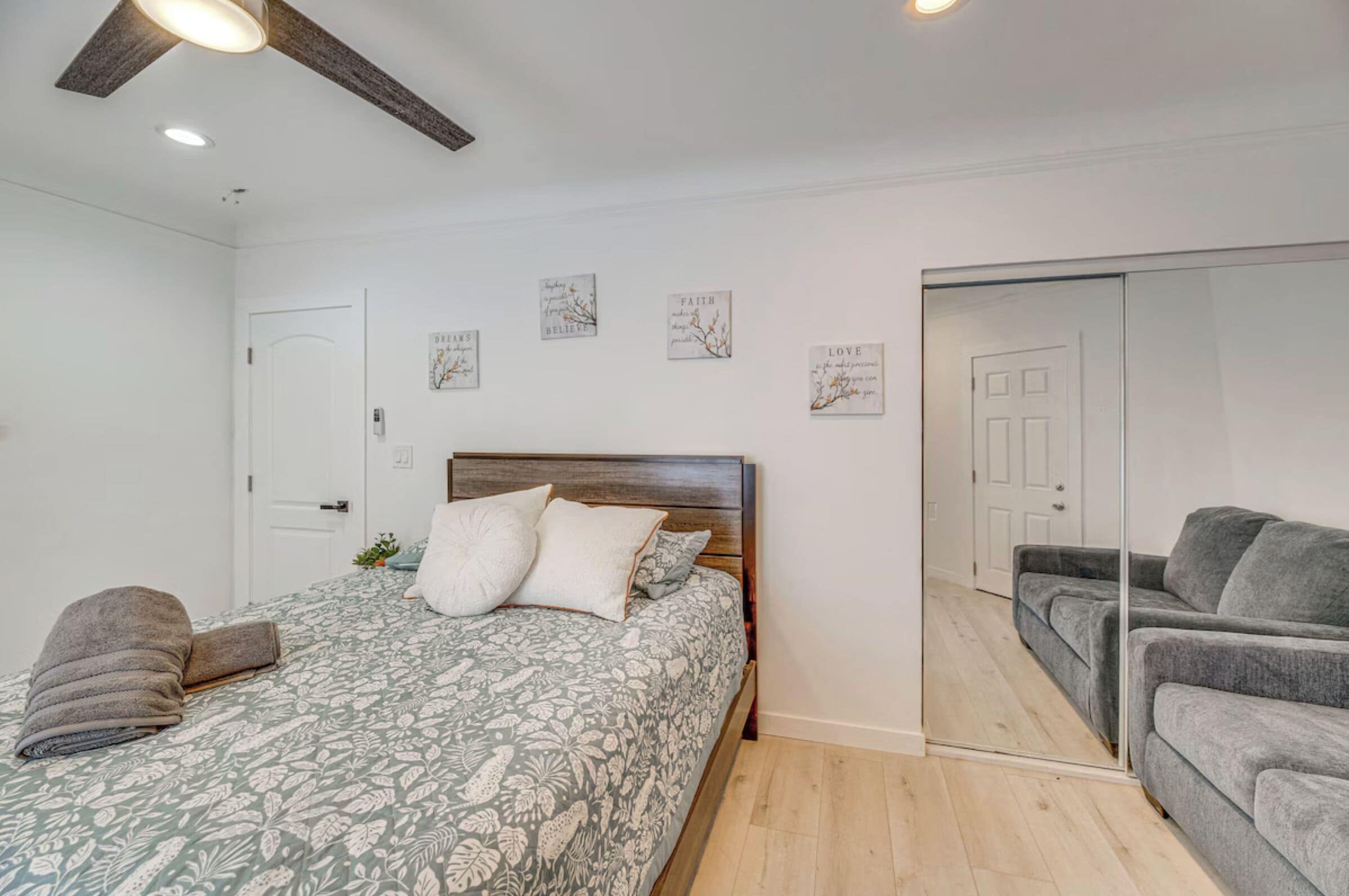A bedroom with a bed, a grey sofa, a wooden ceiling, and a door.