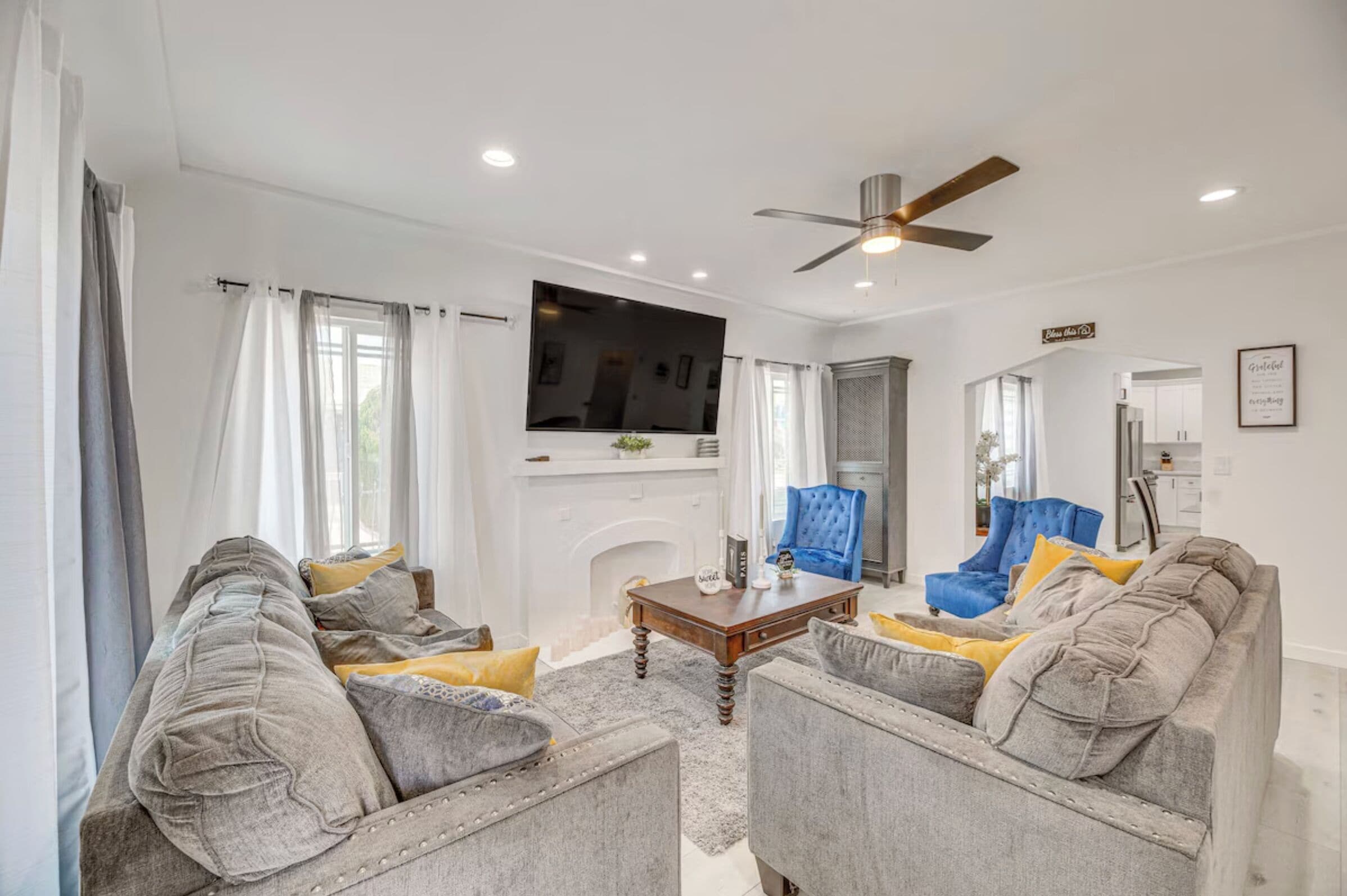 A living room with a fireplace, a television mounted above it, and a ceiling fan.