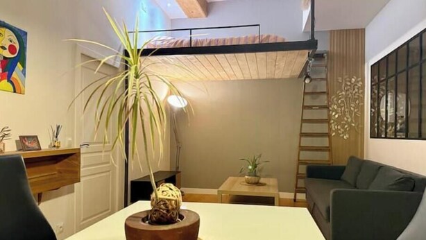 Un saló modern amb una taula de menjador, un sofà, una planta en test i una escala adossada a la paret.