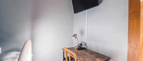 A room with a bed, a desk with a chair, a television mounted on the wall, and a wooden cabinet.