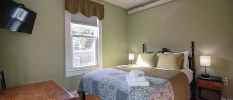 A bedroom with a bed, bedside tables, a desk, a window with curtains, and a television mounted on the wall.