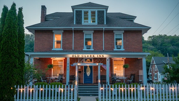 A two-story brick building with a porch, a sign reading 'Old Clark Inn,' and a white picket fence. - Old Clark Inn (Marlinton)