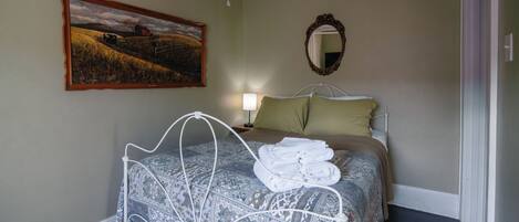 A bedroom with a bed, a painting, a mirror, and a bedside lamp.