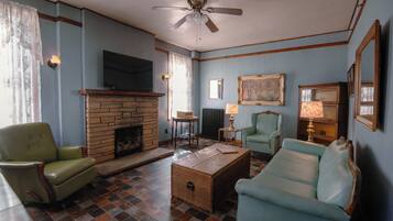 Una sala de estar con chimenea, televisor, ventilador de techo y piso a cuadros.