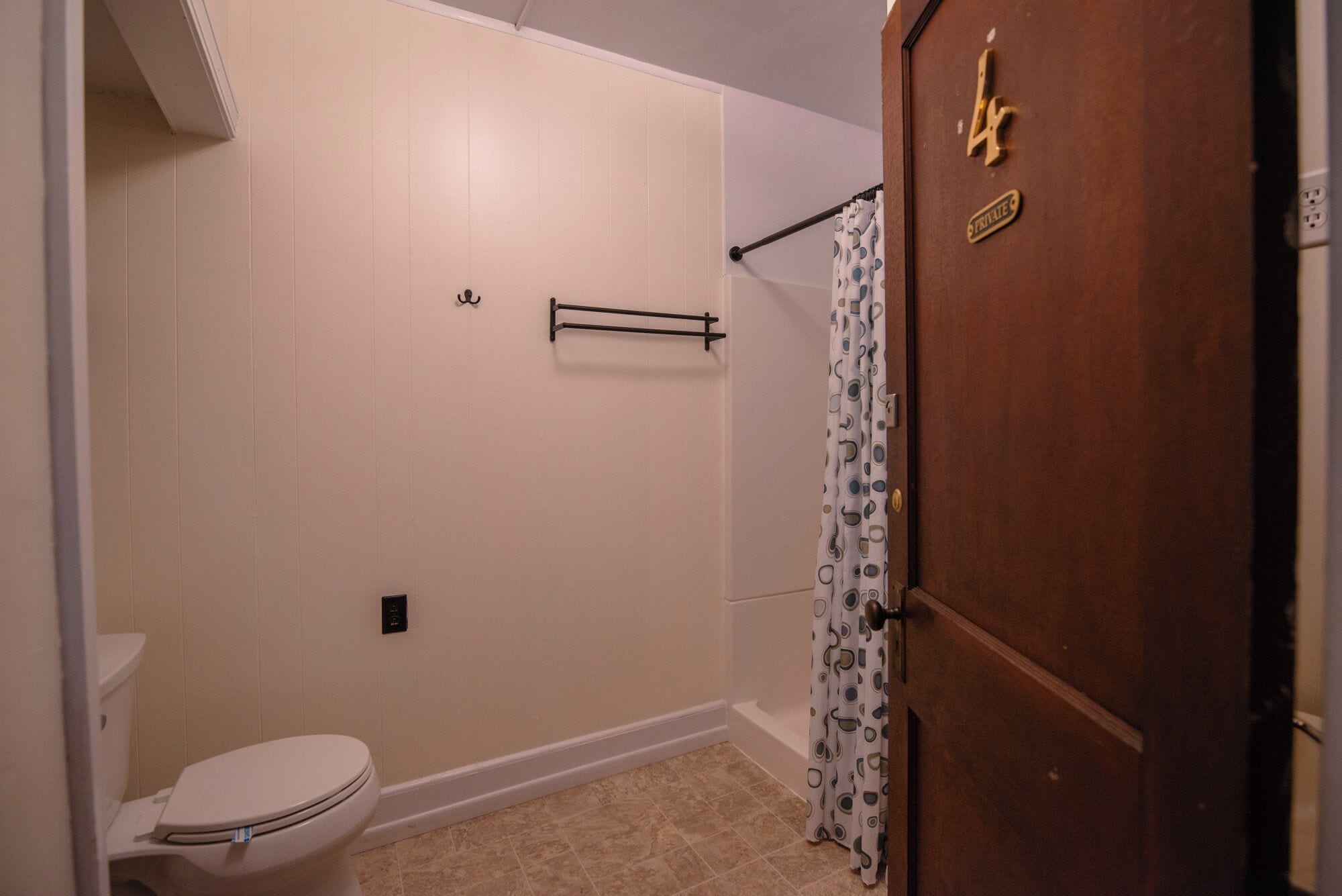 A bathroom with a toilet, shower curtain, towel rack, and a door with a number plate.