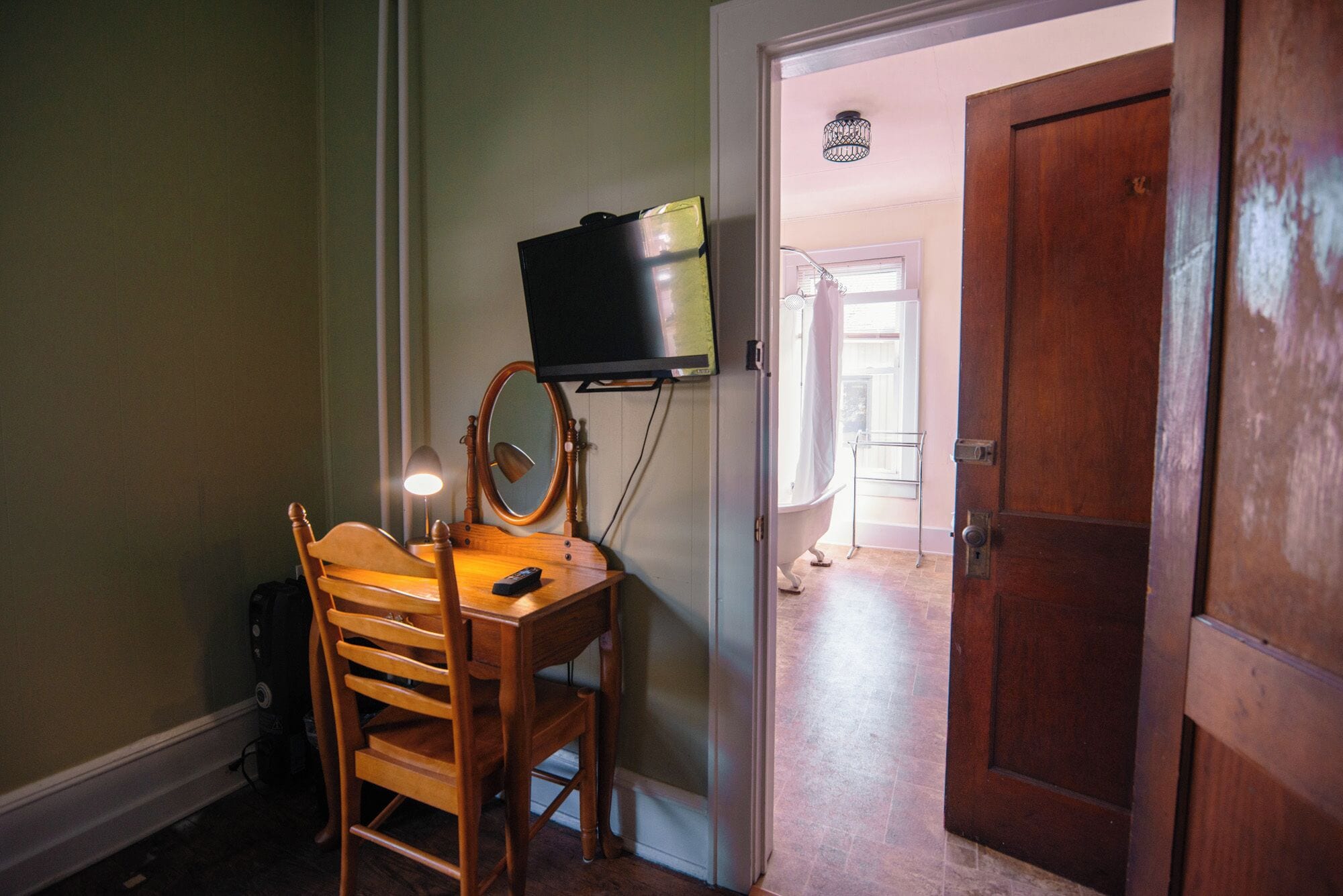 Een kamer met een houten stoel, een aan de muur bevestigde televisie, een spiegel en een houten deur.