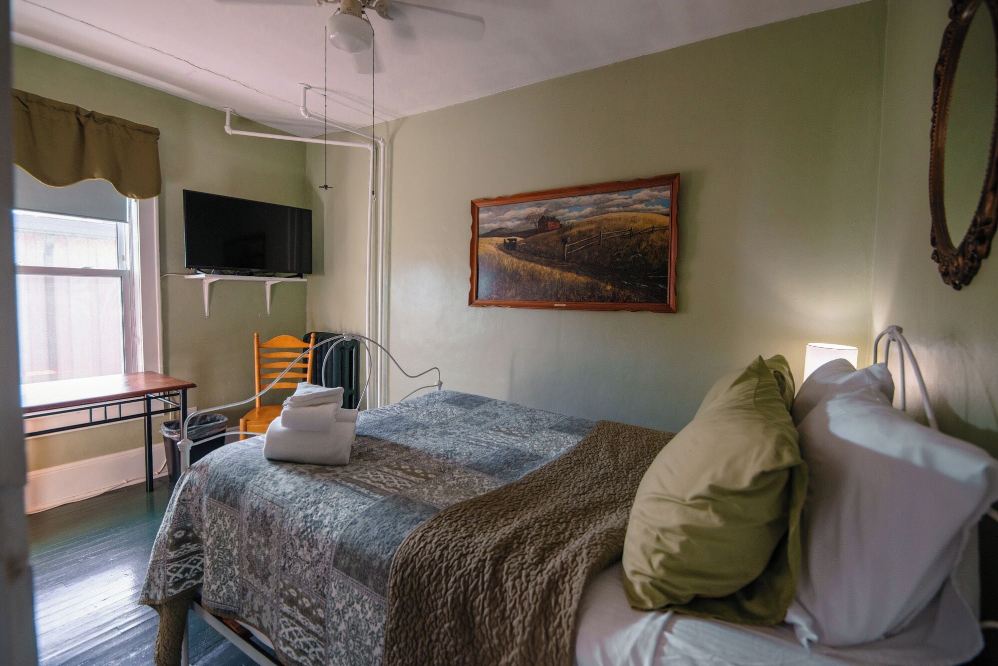 A bedroom with a bed, a chair, a TV, a painting, and a window.