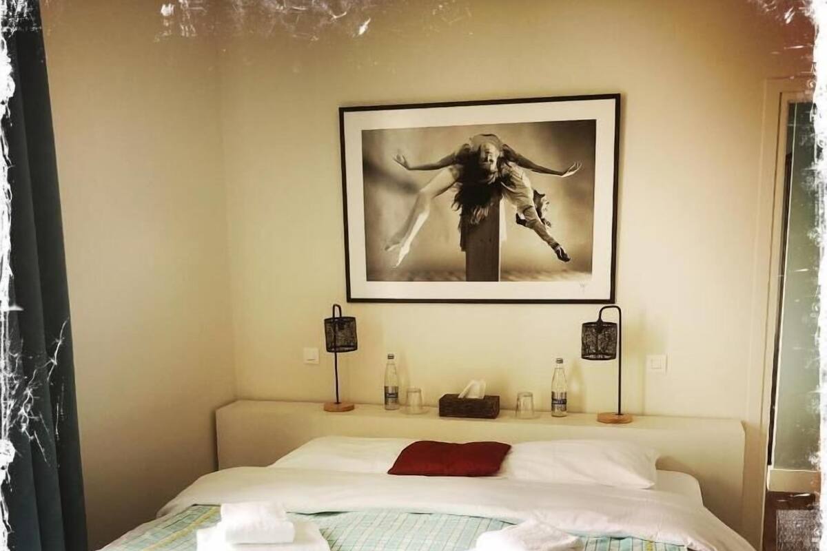 A hotel room with a bed, pillows, a framed picture on the wall, bedside lamps, and a nightstand with a bottle and a tissue box.