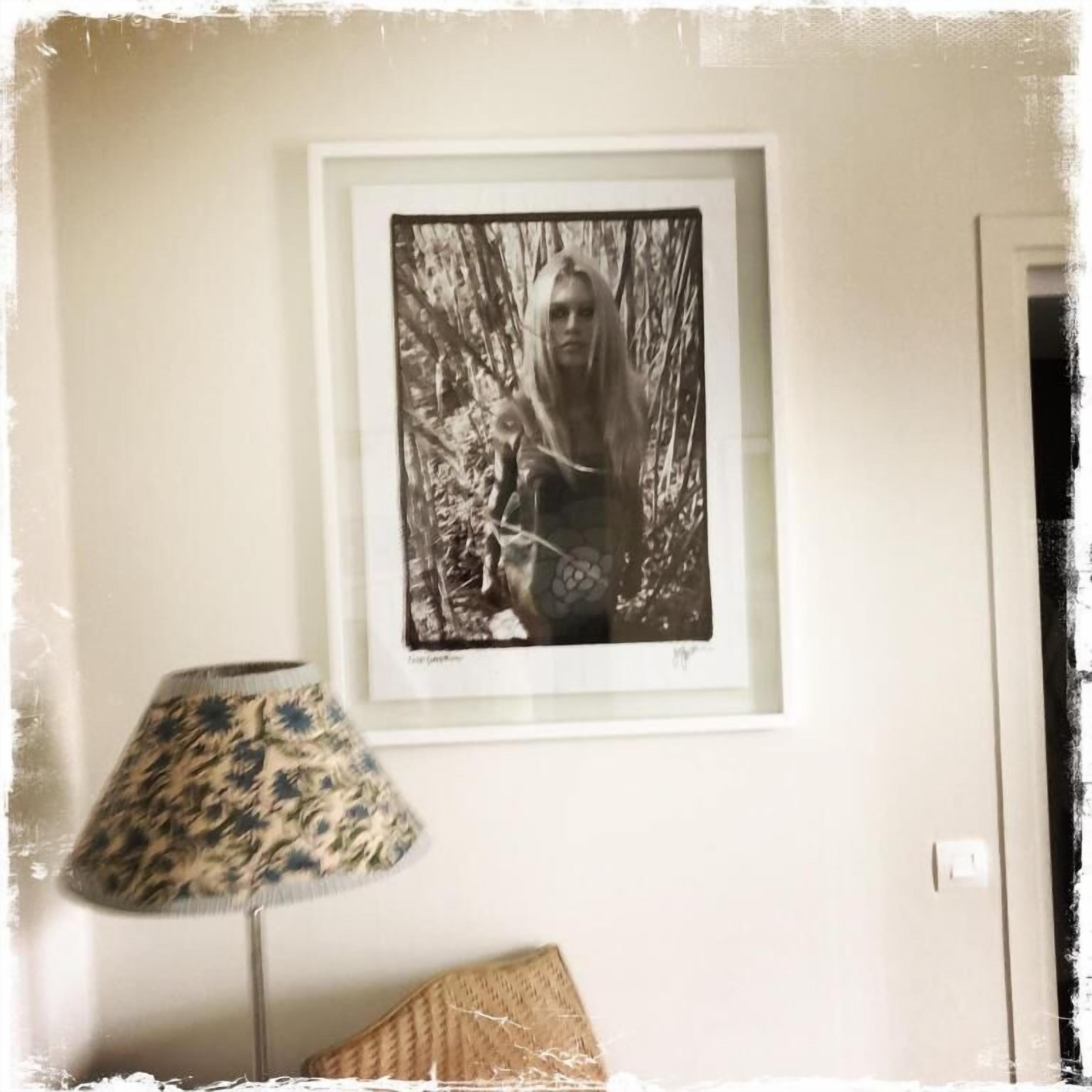 A framed black and white photograph on a wall, a lamp with a patterned shade, and a partially visible door.
