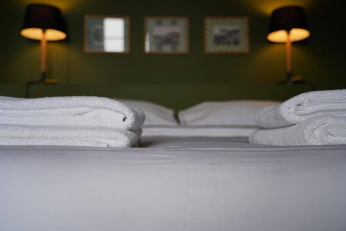 A neatly made bed with folded white towels, two wall-mounted lamps, and framed pictures on the wall.