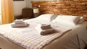 Une chambre d’hôtel avec un lit, une tête de lit, un tableau encadré au mur et une fenêtre avec des rideaux.