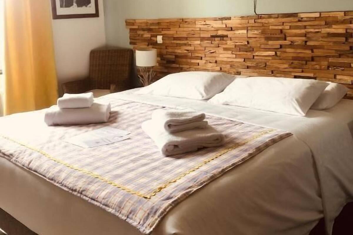 A hotel room with a bed, a headboard, a framed picture on the wall, and a window with curtains.