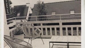 Un balcon d’hôtel avec des chaises en osier, une table et un pot de fleurs.