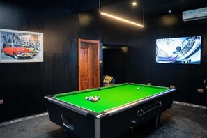 A pool table with balls, a framed painting, a wooden door, and a TV screen. - The Mason By Trovardig (Abuja)