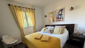 Un dormitorio ordenado con cama, una silla, una mesita de noche y un ventanal con cortinas.