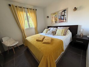 A neatly arranged bedroom with a bed, a chair, a nightstand, and a window with curtains. - Between sea, pool and maquis, T2 with panoramic view (Propriano)