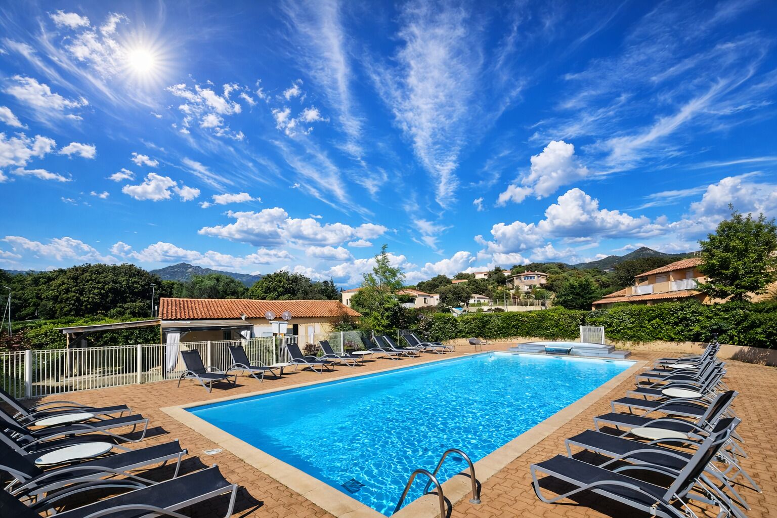 A swimming pool with lounge chairs, a clear sky, and a mountainous backdrop.
