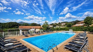 Una piscina con sillas de descanso, cielo despejado y montañas al fondo.