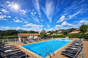 Ein Schwimmbecken mit Liegestühlen, blauem Himmel und einem Bergpanorama im Hintergrund.