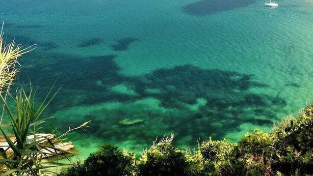 Vista costera con agua turquesa cristalina, barcos y montañas al fondo.