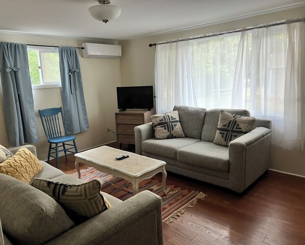 Una sala de estar con sofá, sillón, mesa de centro, televisor y ventana con cortinas.