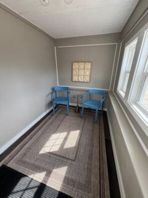 Una habitación con ventana, una silla azul, una mesita y una alfombra estampada.