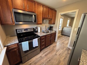 A modern kitchen with wooden cabinets, stainless steel appliances, granite countertops, and a visible clock.