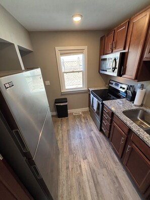 A kitchen with a stainless steel refrigerator, a microwave, a stove, and wooden cabinets. - Modern 2 Bed 1 Bath Friendly Morningside Area (Sioux city)
