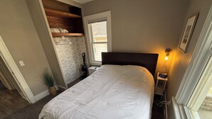 A bedroom with a bed, a nightstand, a lamp, a window, and a door. - Modern 2 Bed 1 Bath Friendly Morningside Area (Sioux city)