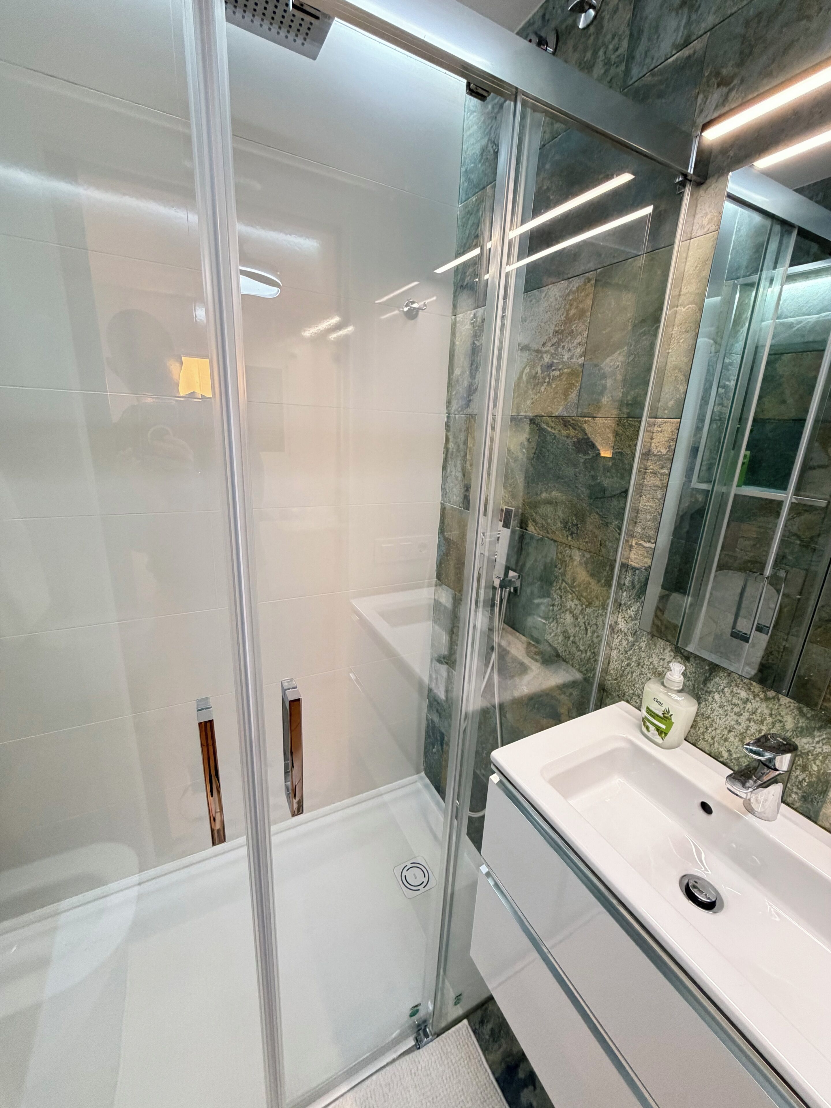 A modern bathroom with a glass-enclosed shower, a white sink, and a granite countertop.