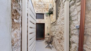 Un callejón estrecho con una puerta, una pequeña mesa con sillas y una planta en maceta.
