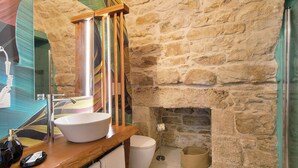 Un baño con pared de piedra, un lavabo blanco, encimera de madera y chimenea de piedra.