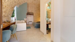 Una habitación con pared de piedra, una mesa de comedor de madera con sillas, un sofá blanco y una pequeña kitchenette.