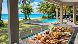 Zona pranzo all'aperto con vista sull'oceano, una piscina e palme.